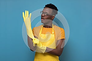 Young african american man cleaning using gloves standing on yellow wall