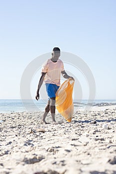 Young African American man collects trash on a sunny beach