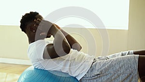 Young African American man doing sit-up exercise with Swiss ball at gym. Male fitness model performing a crunch at