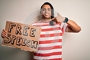 Young african american man with dreadlocks holding banner with free speech message protest with surprise face pointing finger to