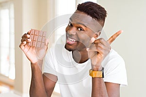 Young african american man eating chocolate bar very happy pointing with hand and finger to the side