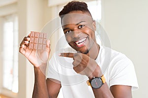 Young african american man eating chocolate bar very happy pointing with hand and finger