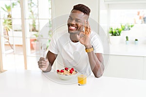 Young african american man eating healthy breakfast in the morning doing ok sign with fingers, excellent symbol