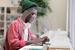 Young African American man freelancer working on laptop using public library as workspace