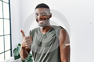 Young african american man getting vaccine showing arm with band aid smiling happy and positive, thumb up doing excellent and