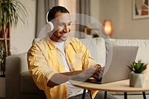 Young African American man in headphones working online, using laptop at home office, copy space