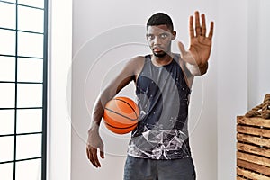Young african american man holding basketball ball at home with open hand doing stop sign with serious and confident expression,