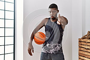Young african american man holding basketball ball at home pointing with finger to the camera and to you, confident gesture