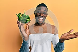Young african american man holding bowl with small green peppers celebrating achievement with happy smile and winner expression