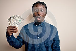 Young african american man holding bunch of dollars banknotes over isolated white background scared in shock with a surprise face,