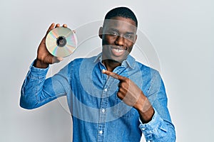 Young african american man holding compact disc smiling happy pointing with hand and finger