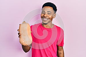 Young african american man holding healthy fresh pumpkin looking positive and happy standing and smiling with a confident smile