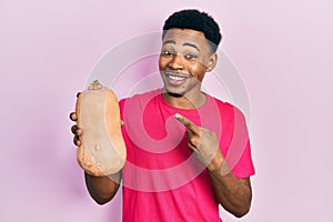 Young african american man holding healthy fresh pumpkin smiling happy pointing with hand and finger