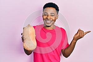 Young african american man holding healthy fresh pumpkin smiling happy pointing with hand and finger to the side