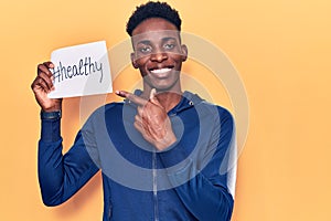 Young african american man holding healthy hashtag paper smiling happy pointing with hand and finger