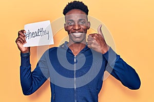 Young african american man holding healthy hashtag paper smiling happy and positive, thumb up doing excellent and approval sign