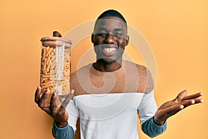 Young african american man holding jar of macaroni pasta celebrating achievement with happy smile and winner expression with