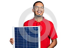 Young african american man holding photovoltaic solar panel celebrating crazy and amazed for success with open eyes screaming