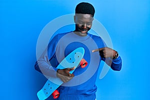 Young african american man holding skate smiling happy pointing with hand and finger