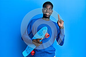 Young african american man holding skate smiling with an idea or question pointing finger with happy face, number one