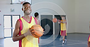 Young African American man holds a basketball in a gym, with copy space