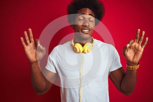 Young african american man listening to music using headphones over isolated red background relax and smiling with eyes closed