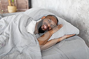 Young African American man lying in bed looking at camera