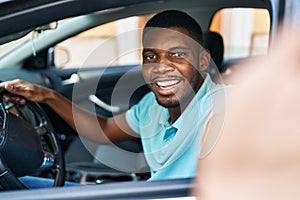 Young african american man making selfie by the camera sitting on car at street
