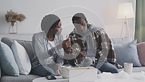 Young african american man measuring temperature with oral thermometer, caring wife feeling worried and disturbed