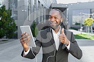 A young African American man near the office in headphones and talking on a video call on a tablet