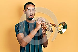 Young african american man playing trumpet afraid and shocked with surprise and amazed expression, fear and excited face