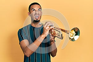 Young african american man playing trumpet angry and mad screaming frustrated and furious, shouting with anger looking up