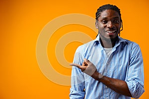 Young african american man pointing at copy space over yellow background