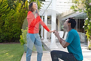 Young african american man proposing biracial girlfriend while kneeling in garden