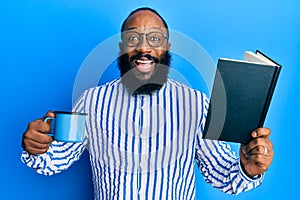 Young african american man reading book and drinking a cup of coffee smiling and laughing hard out loud because funny crazy joke