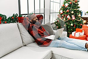 Young african american man relaxed with hands on head sitting by christmas tree at home
