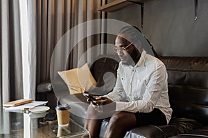 Young African American man relaxing on soft at home, texting messaging on smartphone. man using mobile phone chatting