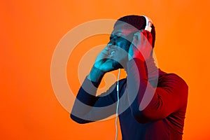 Young african-american man`s listening to music in headphones in neon light. Male portrait. Concept of human emotions