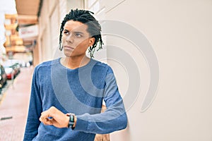 Young african american man with serious expression leaning on the wall at street of city