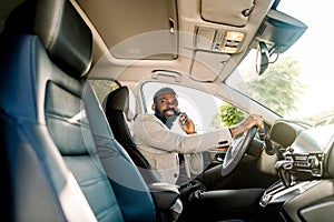 Young African American man in smart casual business wear, using phone sitting in the car, side view