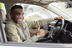 Young african american man smiling while driving a car showing thumbs up recommending something good.