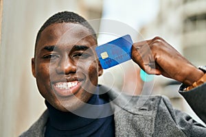 Young african american man smiling happy holding credit card at the city