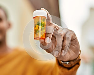 Young african american man smiling happy holding pills at the city