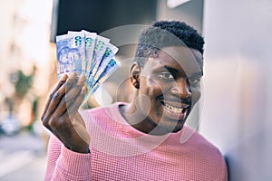 Young african american man smiling happy holding south africa rands at the city photo