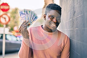 Young african american man smiling happy holding south africa rands at the city