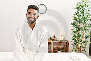 Young african american man smiling happy sitting on massage table at beauty center