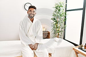 Young african american man smiling happy sitting on massage table at beauty center