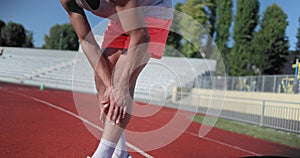 Young african american man in sportswear doing self massage to relieve joint pain while standing in stadium