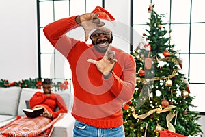 Young african american man standing by christmas tree smiling making frame with hands and fingers with happy face