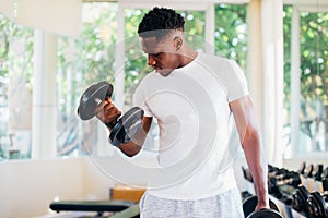 Young African American man standing and lifting a dumbbell with the rack at gym